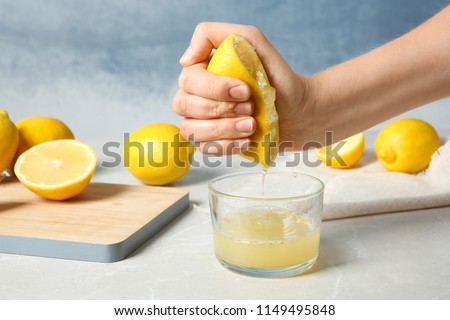 Woman squeezing lemon juice into glass on table Royalty-Free Stock Photo #1149495848