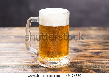Mug of cold pale beer placed on a rustic wooden table with copy space
