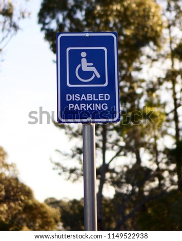 Disabled parking sign in blue and white with blurred grey sky background