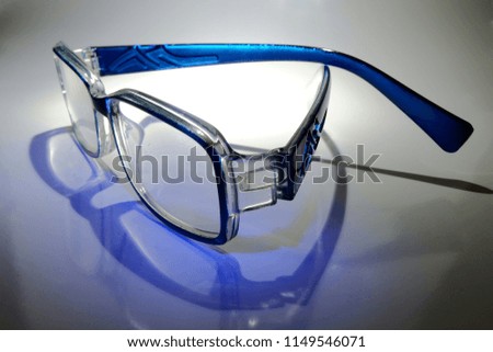 Colorful glasses are placed on white paper that reflects the light and shadow of the blue glasses.