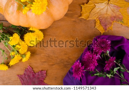 Pumpkin, violet and yellow chrysanthemum flowers and dry autumn leaves on a weathered wooden background (copy space in the center, top view, flat lay)