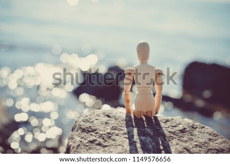 A wooden man sitting on a stone on the beach.
