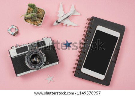 Retro camera with toy plane on pastel pink background with travel diary and emprt screen smart phone, Summer vacation concept