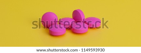 Several large bright pink tablets on a yellow background. In the center of the image.