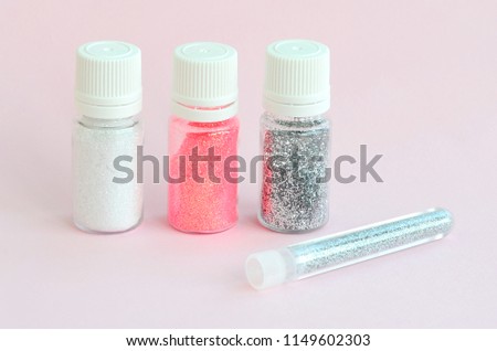 Colorful glitters lies on pastel pink background. Many round jars with multi-colored bright sparkles for nail polish. Sparkling sequins