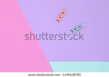 Two colored wooden pegs lie on texture background of fashion pastel violet, blue and pink colors paper in minimal concept