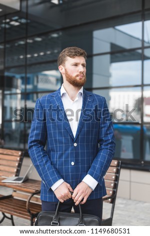 a businessman in a suit with a portfolio is standing against a background of glass buildings