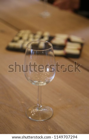 square pieces of solid white yellow cheese on a brown board for tasting on a table and an empty wine glass