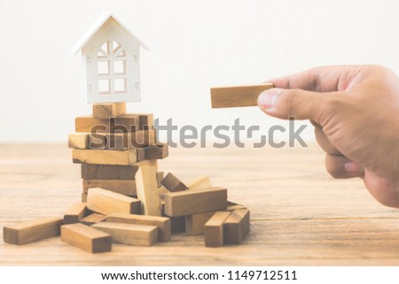 Hand holding wood block with model white house on wood block game. Investment risk and uncertainty in the real estate housing market. Property investment and house mortgage financial concept.