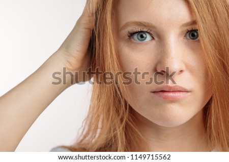 serious redhair model with blue eyes.holding her head. close up cropped photo.a nice girl is unhappy to have red hair