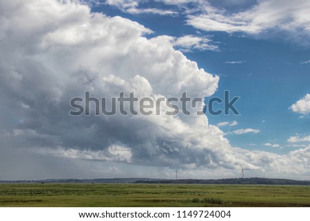 Stormclouds over marsh with windmills in the distance.