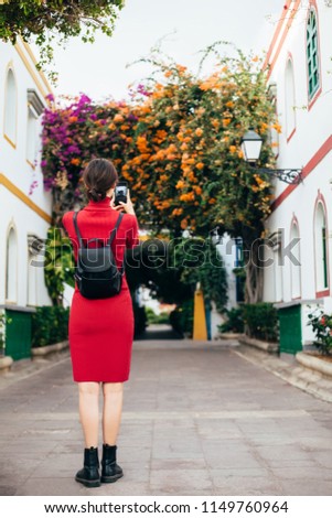 Young traveler woman taking a photo of cozy spanish street with colorful flowers on her mobile phone 