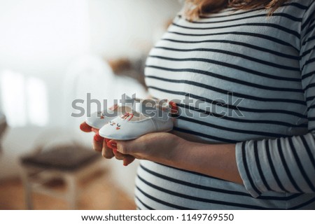 Pregnant mother holding small shoes for a baby. Waiting for the baby. The loving parents. Copyspace included.