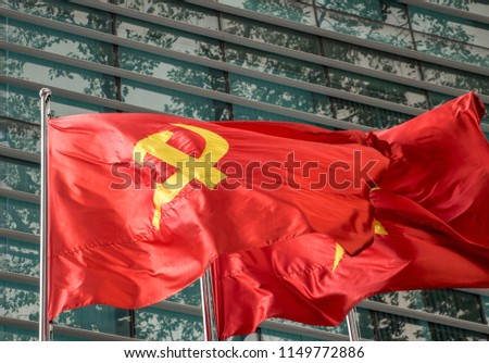 The red flag with communist symbols of a sickle and a hammer flying by building.The Red flag with a five-pointed star flutters on the pole.