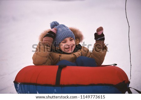 cheerful little boy in winter walks in the cold on an inflatable sled