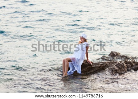 Charming young lady in a white dress among the sea rocks