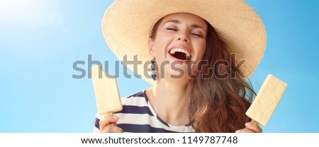 smiling trendy woman in straw hat against blue sky with two ice cream