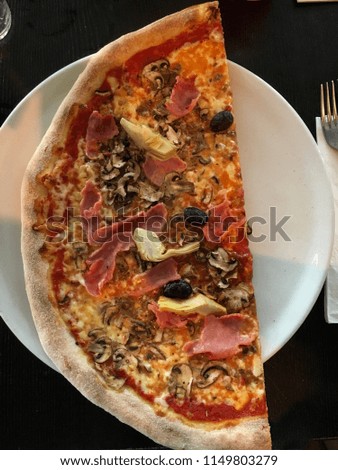 One half of the round pizza on the white plate. Pizza  capricciosa with cheese, ham, mushrooms, olives and artichokes.