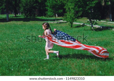 A happy girl runs along the green grass and waving an American flag