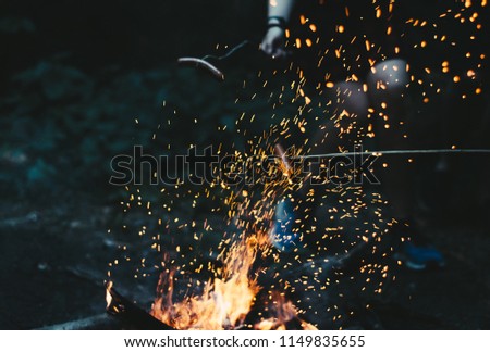 A picture of people frying their sausages on the fire.