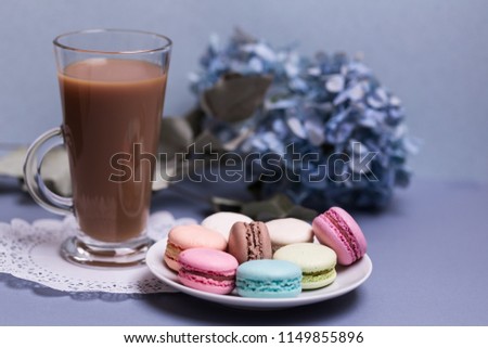 Close-up morning glass cup of coffee with milk, cake macaron and flower on blue table. Beautiful dessert