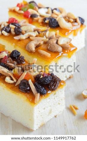 Three pieces of fruitcake topped with mix fruits and Cashew nuts on wooden cutting board