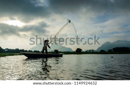 An unknown fisherman standing at the boat and throw a net at the lake to find fish.Silhouette.Selective focus