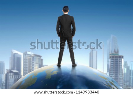 Rear view of asian businessman standing on earth and looking at cityscape view with blue sky background