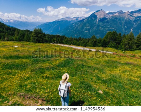 Aerial view of female tourist with backpack standing on green grass meadow and enjoying beauty of nature. Hipster girl wanderlust making walking route while recreating in National Park during summer