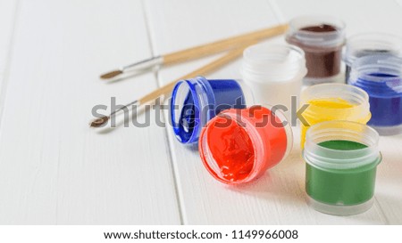 Several overturned jars of gouache and a brush on a white wooden table. Creative kit.