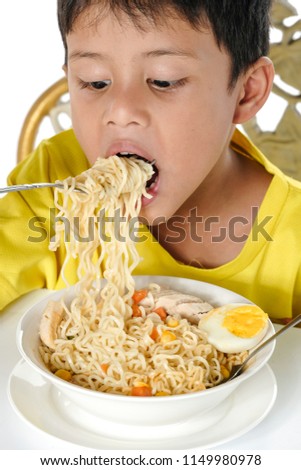 A young malay boy sitting while enjoy having instant noodles isolated on white background