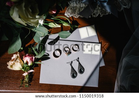 Wedding accessory bride. Stylish earrings, gold rings, flowers, garter on table standing on wooden background. Letters from the bride and groom. flat lay. top view.