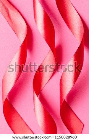 Curled red satin ribbons on pink background, vertical