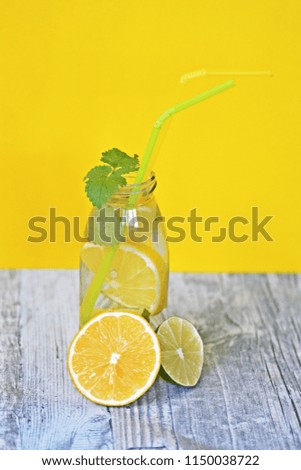 Pieces of lemons, mint and limes in a bottle full of water as a fruity refreshment in summer against a plain background