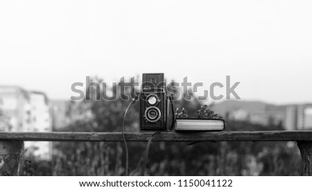 Vintage film camera with book and flowers on park bench behind the green city landscape