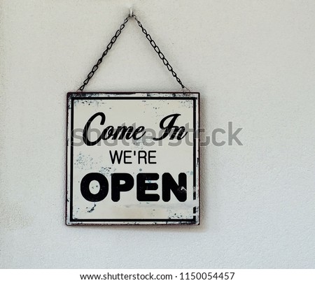Come in we are open,  black and white  retro sign on white wall of a store.