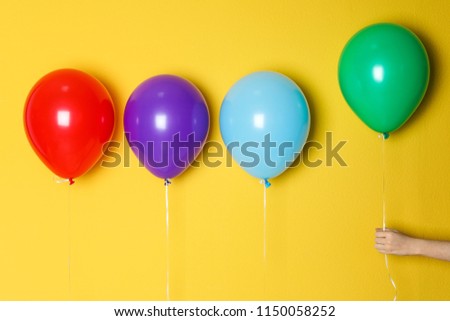 Woman holding green balloon next to others on color background. Celebration time