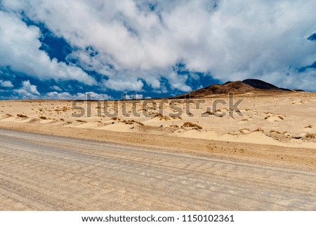 white roads in the sandy desert under the blue sky with clouds in the Canary Island of Fuerteventura