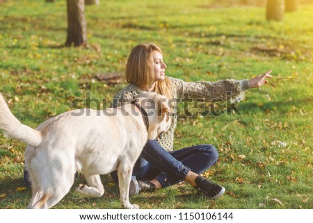 beautiful blonde is sitting on the grass in the park and playing with her dog labrador