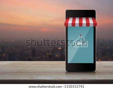 Modern smart mobile phone with online shopping store graphic and open sign on wooden table over blur of cityscape on warm light sundown, Business internet shop online concept