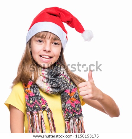 Half-length portrait of caucasian girl wearing Santa Claus hat. Schoolgirl looking at camera and making thumb up gesture. Holiday Christmas concept - happy cute child isolated on white background.