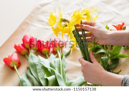 florist business. woman hands arranging a spring flower bouquet from assortment of yellow narcissus and red tulips