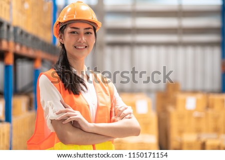 Young warehouse operator portrait. Young chinese woman in safety hat holding tablet with bottle warehouse in background. Royalty-Free Stock Photo #1150171154