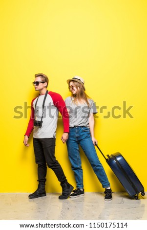 Portrait of smiling travel young couple while standing with suitcases and photo camera isolated over yellow background