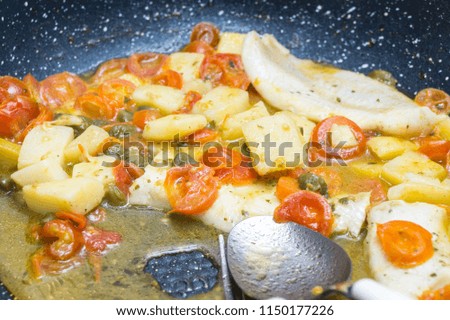 cod cooked in a pan, with tomato, potatoes and capers
