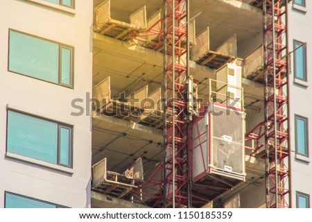 Elevator in high building construction site for transport construction workers up unfinished buildings. Passenger and material hoist transport platform for vertical transportation of man and material. Royalty-Free Stock Photo #1150185359