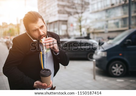 Busy man is in a hurry, he does not have time, he is going to eat snack on the go. Worker eating, drinking coffee, talking on the phone, at the same time. Businessman doing multiple tasks.  Royalty-Free Stock Photo #1150187414