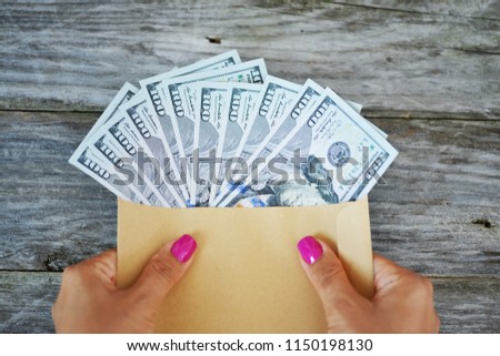 Hands of a woman holding an envelope full of US dollars banknotes
