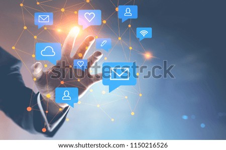 Hand of businessman touching a glowing polygons speech bubbles hologram with social media icons over a blurred blue background. Toned image double exposure mock up