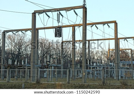 part of a power plant with poles, transformers and wires behind a fence